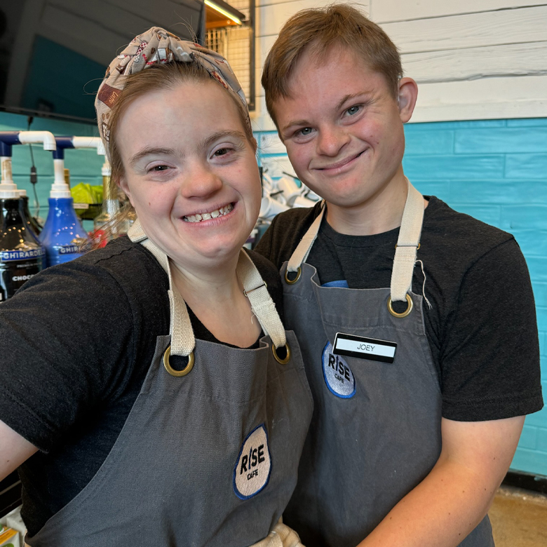 Kelley and Joey smiling in their Rise Up Cafe aprons